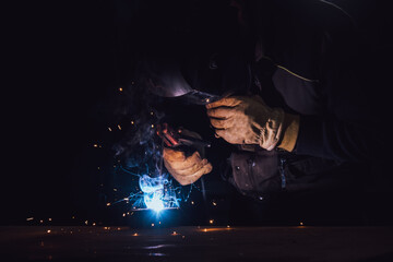 Welder welding a metal plate with an electrode in the dark of a factory