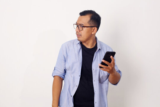 Adult Asian Man Looking Sideways When Holding His Mobile Phone With Serious Expression. Isolated On White Background