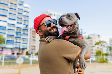 portrait of happy man in red hat and sunglasses with american terrier in dogs walking area park in...