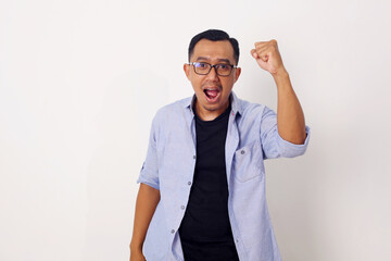 Happy energetic young Asian man yelling and clenching fists isolated on white studio background