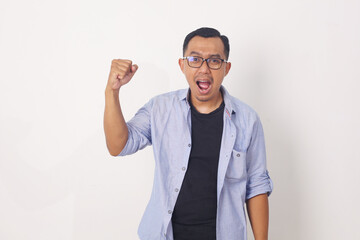 Happy energetic young Asian man yelling and clenching fists isolated on white studio background