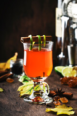 Hot punch, grog, winter warming cocktail drink with dark rum, port, honey, lime juice, tea, cinnamon and cloves in glass on vintage wooden background in autumn decoration