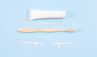 Toothpaste, bamboo toothbrush, dental floss on soft blue.
