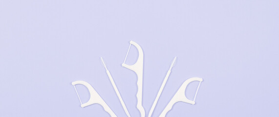 Dental floss and toothpicks on a soft lilac background.
