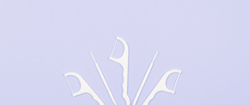 Dental floss and toothpicks on a soft lilac background.