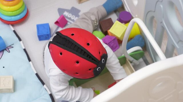 Cute toddler playing with soft montessori building blocks in baby playpen with play mat for babies and toddlers, 8 month old baby boy wearing safety helmet enjoy playing time in kids activity centre.