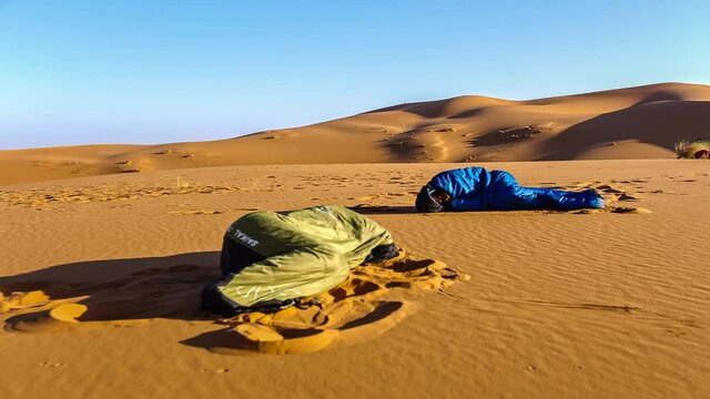 Time lapse shot of two people inside bedroll sleeping on sand of wild Sahara desert in Morocco,Africa - Adventure trip in Wilderness