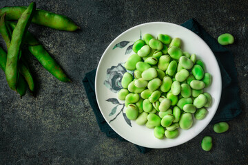 green broad beans  in a white plate against dark background