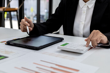 A woman looking at a tablet at a screen showing company financial status chart and presses a calculator to check, a finance worker is checking documents. Concept of company financial management.