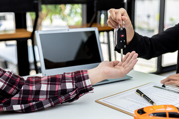 A car rental company employee is handing out the car keys to the renter after discussing the rental details and conditions together with the renter signing a car rental agreement. Concept car rental.