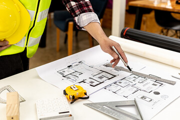 The architect-engineer stood holding a hat and pointed a pen to the floor plan of the house on the...