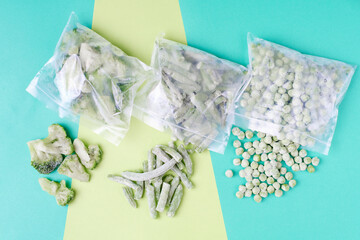 Frozen vegetables in plastic bags on green background, top view.