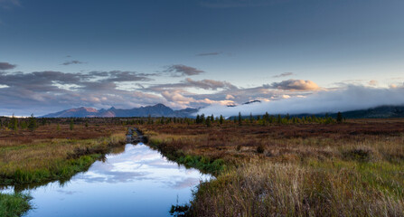 Russia. Magadan Region. A beautiful forest lake against the backdrop of the Big Anngachak mountain range. Autumn in the vicinity of Lake Jack London.