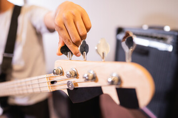 close up of a bassist's hand tuning an electric guitar bass string before use
