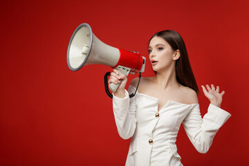 High fashion photo of elegant young model with Megaphone in white suit, pants, trousers top jacket. Beautiful young woman, slim figure. Studio shot. Red background