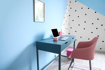 Cup, laptop, calendar on table and chair near color wall