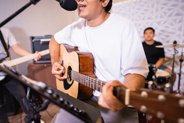 close up of a male vocalist singing while playing an acoustic guitar