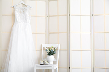 Beautiful dress and chair with shoes and flowers in light room