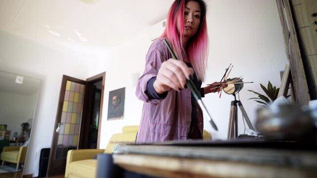 Pink haired korean visual artist painting at studio home
