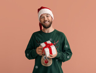 Young man in Santa Claus hat and with Christmas gift on color background