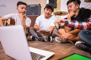 young band members chatting and using laptops together while sitting relaxing on the floor writing song arrangements