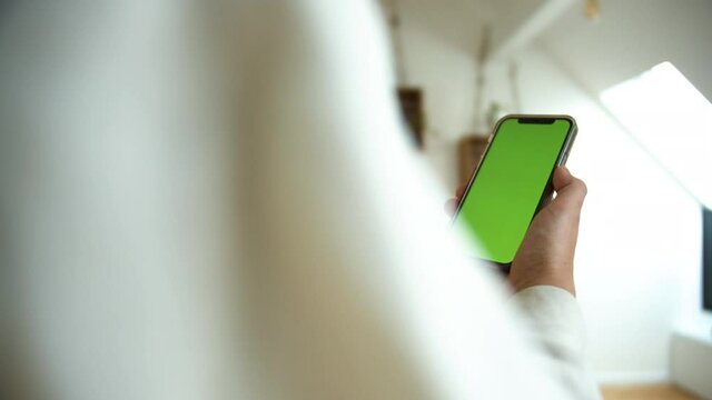 Side view of a causal dressed man holding smartphone with green screen chroma key in white home background.