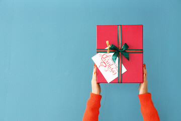Woman holding Christmas gift box on color background