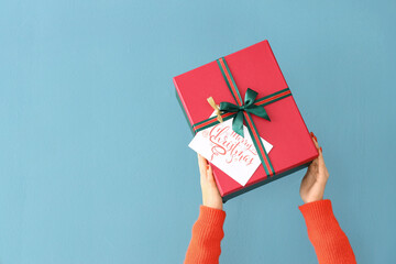 Young woman holding Christmas gift box on color background