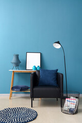 Modern armchair, table with blank frame and floor lamp near color wall
