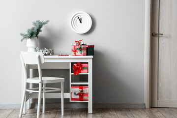 Workplace with different Christmas gift boxes and vase with fir tree branches near white wall