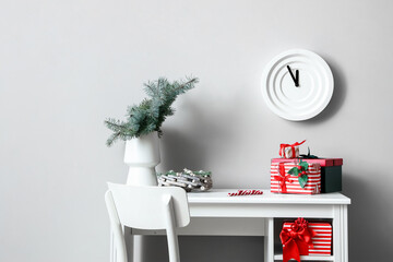 Workplace with different Christmas gift boxes and vase with fir tree branches near light wall