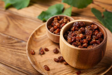 Bowls with tasty raisins on wooden background, closeup