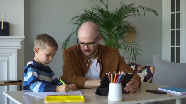 Online education of preschoolers at home. Little preschooler boy draws picture and gives father high five at lesson via contemporary tablet at table spbd
