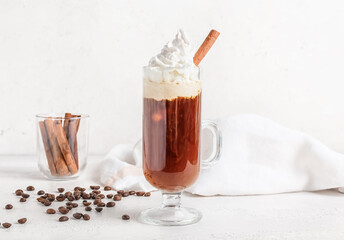 Glass cup of tasty coffee with cinnamon and beans on light background