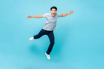 Young Asian man jumping in mid air with hands outstretched on isolated light blue background
