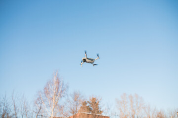 An electric drone is flying in the blue sky. 3D illustration. Drone: 3D model. Background: photopanorama.