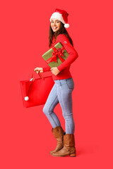 Beautiful young woman with Christmas gift and shopping bag on color background