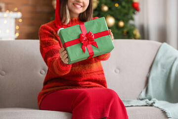 Beautiful young woman with gift at home on Christmas eve