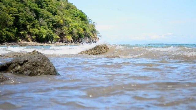 Beautiful lush shoreline of Costa Rica's west coast captured in full HD. Low angle close to the water while small waves crash on rocks with tropical forest in background.