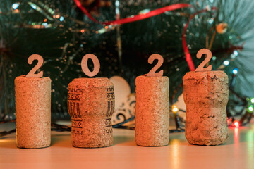 There are wooden numbers 2022 on the champagne and wine corks. On the background of a Christmas tree with lights garlands. Happy New Year and Christmas. Wooden background.