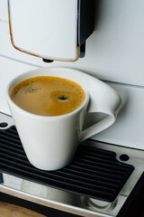 White cup of espresso with thick foam in coffee machine on table, top view from above