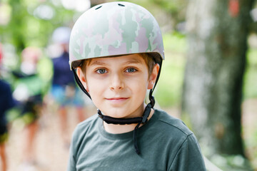School boy in forest adventure park. Acitve child, kid in helmet climbs on high rope trail. Agility skills and climbing outdoor amusement center for children. Outdoors activity for kid and families.