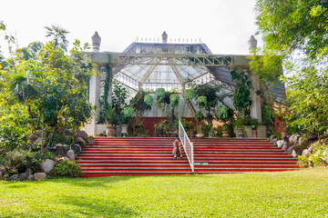 A woman sits and stares at the camera from the red stairs in of the great greenhouse of Puerto Vallarta's botanical garden in Mexico