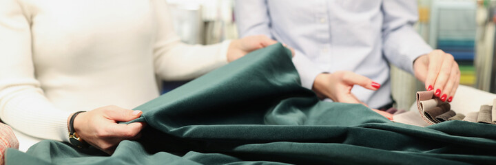 Two women examine fabric of green emerald color