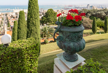A decorative bronze flowerpot with geraniums stands on the railing of the terrace in the Bahai...