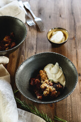 Homemade plum crumble pie with whipped cream in bowl on wooden table. Selective focus