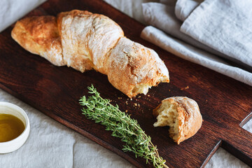 Artisan sourdough bread served with olive oil and thyme on wooden cutting board. Selective focus