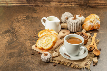 Breakfast concept with a cup of coffee, croissants, milk jug, and decorative crochet pumpkins