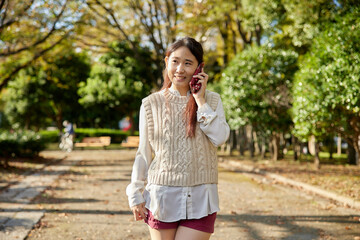 Fototapeta premium 公園の中で電話をかけるアジア人女性