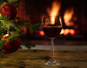 Red wine glass, burning fireplace background. Christmas tree decoration